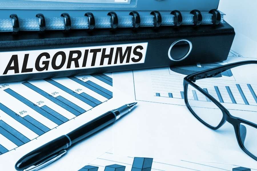 Un grand classeur noir portant l'inscription ALGORITHMS repose sur des documents d'analyse financière et des graphiques.