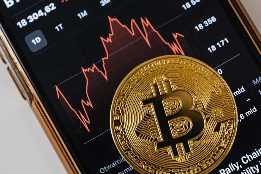 Une pièce physique de Bitcoin en or repose sur l'écran d'un smartphone affichant un graphique boursier rouge, illustrant la volatilité sous réglementation sur les cryptomonnaies.