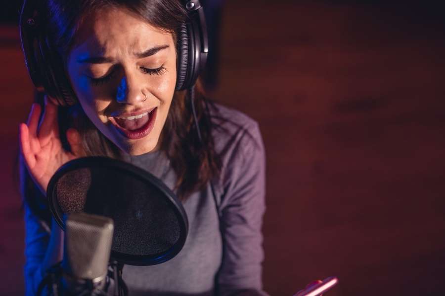 Une jeune femme chanteuse avec un casque audio enregistre sa voix grâce à un générateur de chanson par IA.